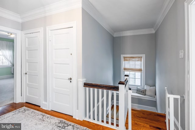 hallway featuring an upstairs landing, a healthy amount of sunlight, crown molding, and wood finished floors