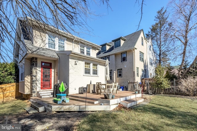 back of property with stucco siding, fence, a yard, roof with shingles, and a wooden deck