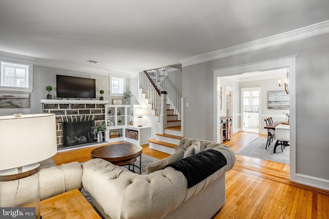 living room featuring stairway, light wood-style flooring, a fireplace, and ornamental molding