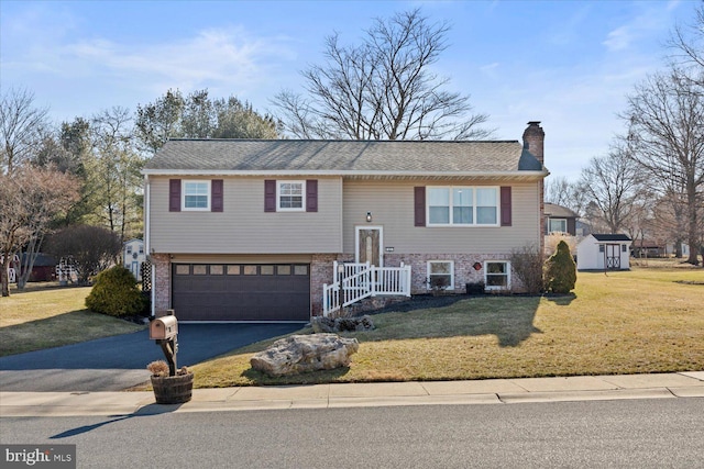 bi-level home with a front lawn, aphalt driveway, an attached garage, brick siding, and a chimney