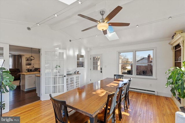 dining area featuring lofted ceiling with skylight, light wood-style flooring, baseboard heating, and ceiling fan