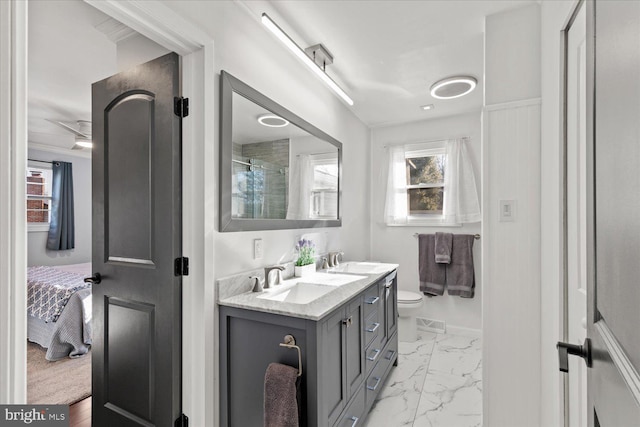 ensuite bathroom featuring double vanity, marble finish floor, a healthy amount of sunlight, and a sink