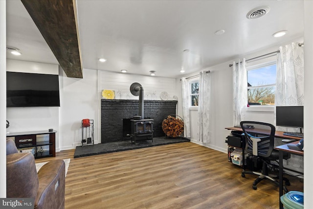 office space with a wood stove, wood finished floors, visible vents, and baseboards