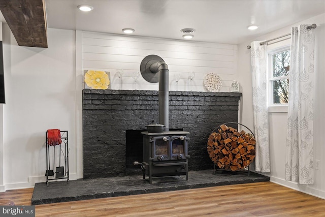 room details featuring visible vents, a wood stove, wood finished floors, and baseboards