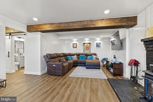 living area featuring a barn door, beam ceiling, baseboards, and light wood-style flooring