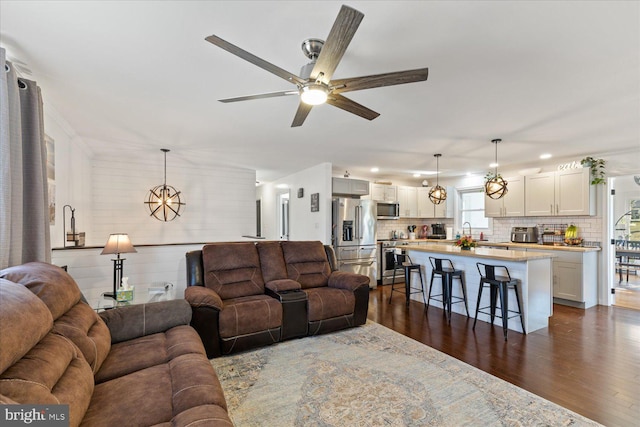 living area featuring ceiling fan with notable chandelier and dark wood-type flooring