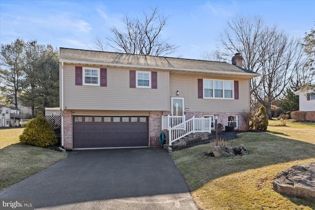 split foyer home featuring driveway, a front yard, an attached garage, brick siding, and a chimney