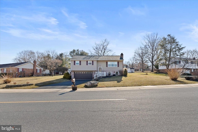 bi-level home featuring a garage, a chimney, concrete driveway, and a front yard