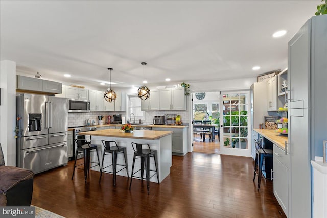 kitchen featuring tasteful backsplash, a kitchen breakfast bar, stainless steel appliances, wood counters, and a sink