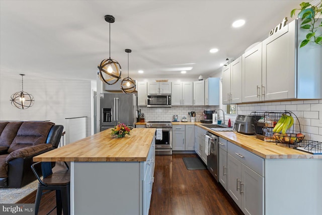 kitchen featuring butcher block countertops, a kitchen breakfast bar, dark wood-style floors, stainless steel appliances, and a sink