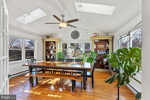 dining area with ornamental molding, vaulted ceiling with skylight, light wood-style floors, baseboard heating, and ceiling fan