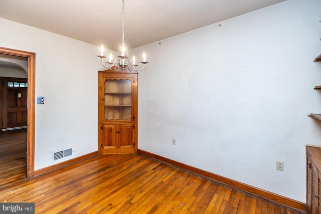 unfurnished dining area featuring visible vents, baseboards, arched walkways, a notable chandelier, and wood-type flooring