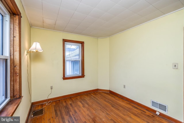 spare room featuring crown molding, wood finished floors, visible vents, and baseboards