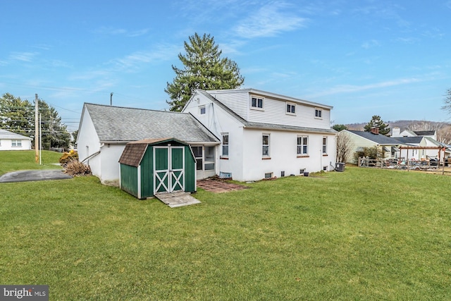 rear view of house featuring an outbuilding, a lawn, a shed, and stucco siding