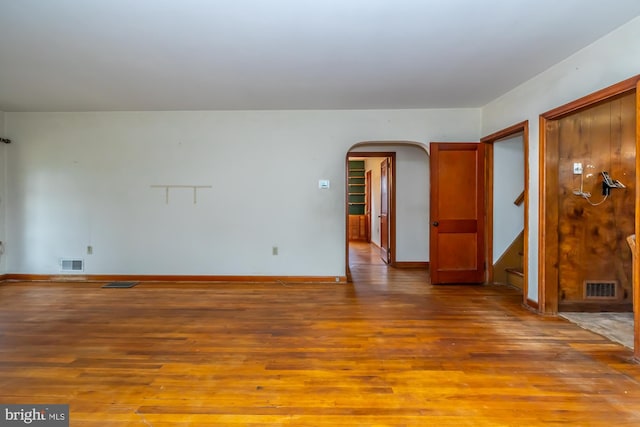 spare room featuring arched walkways, visible vents, and wood finished floors