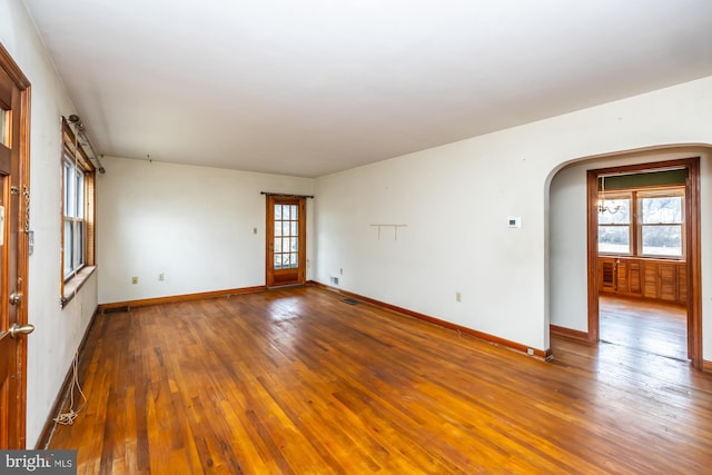 spare room with baseboards, arched walkways, visible vents, and wood-type flooring