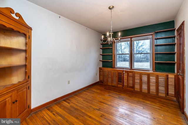 spare room with baseboards, wood-type flooring, and a notable chandelier