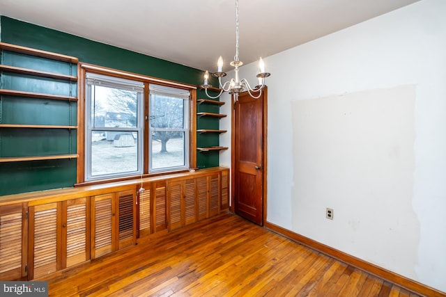 spare room featuring baseboards, wood-type flooring, and a chandelier