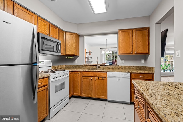 kitchen featuring light tile patterned floors, light stone counters, brown cabinets, appliances with stainless steel finishes, and a sink