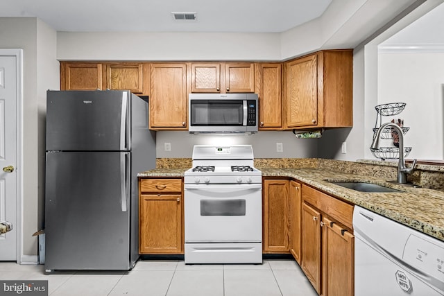 kitchen with a sink, light stone counters, brown cabinetry, and stainless steel appliances