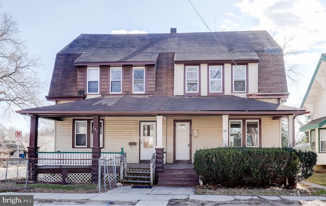 dutch colonial with fence, covered porch, a gambrel roof, and a shingled roof