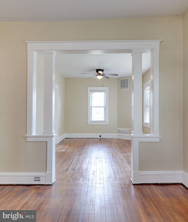 empty room featuring visible vents, hardwood / wood-style flooring, baseboards, and decorative columns