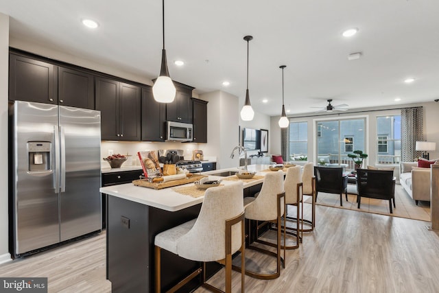 kitchen with light wood finished floors, open floor plan, light countertops, appliances with stainless steel finishes, and a sink