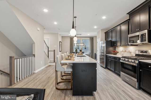 kitchen featuring a breakfast bar area, an island with sink, light countertops, light wood-style floors, and appliances with stainless steel finishes