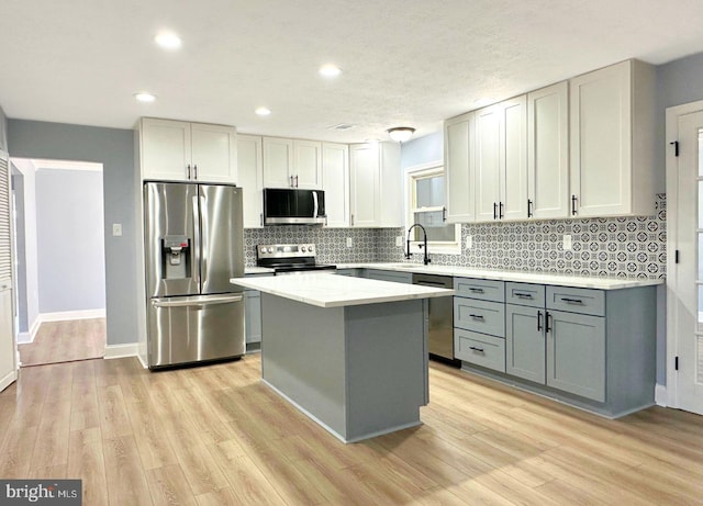 kitchen with gray cabinetry, a sink, a center island, appliances with stainless steel finishes, and light wood finished floors