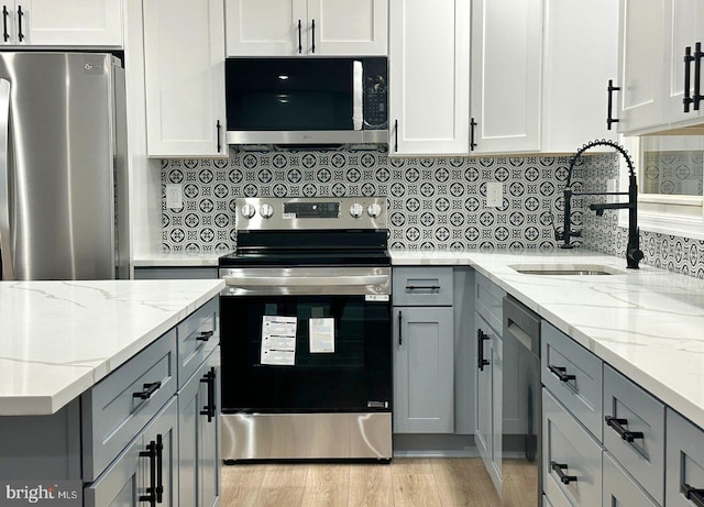 kitchen with light stone counters, light wood finished floors, a sink, gray cabinetry, and stainless steel appliances