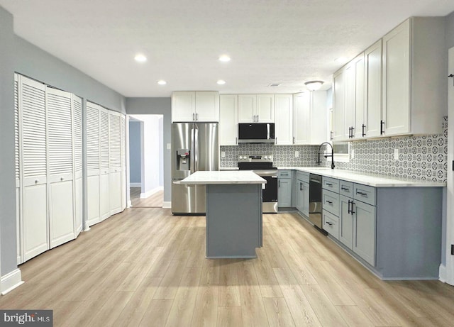 kitchen with gray cabinetry, a kitchen island, appliances with stainless steel finishes, light countertops, and decorative backsplash