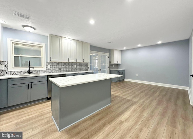 kitchen featuring visible vents, backsplash, dishwasher, gray cabinets, and a sink