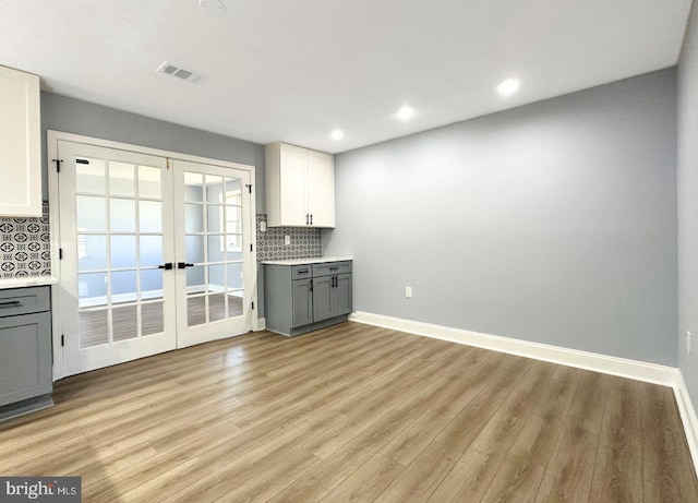 kitchen featuring visible vents, backsplash, gray cabinetry, light wood-type flooring, and french doors