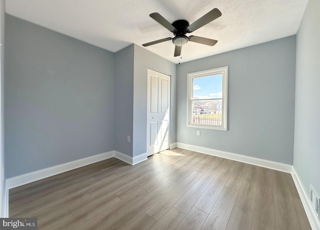 unfurnished bedroom with a ceiling fan, wood finished floors, baseboards, a closet, and a textured ceiling