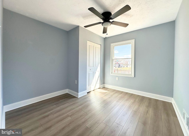 unfurnished bedroom with wood finished floors, baseboards, ceiling fan, a closet, and a textured ceiling