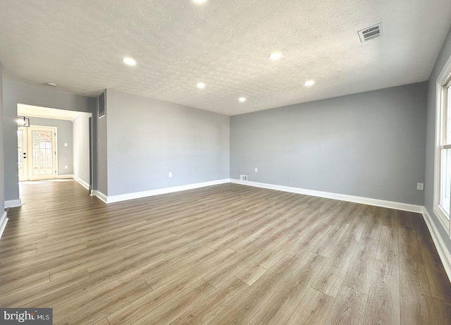 unfurnished room with visible vents, a textured ceiling, baseboards, and wood finished floors