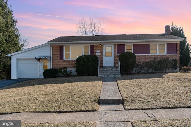 ranch-style home featuring aphalt driveway, a front yard, an attached garage, brick siding, and a chimney