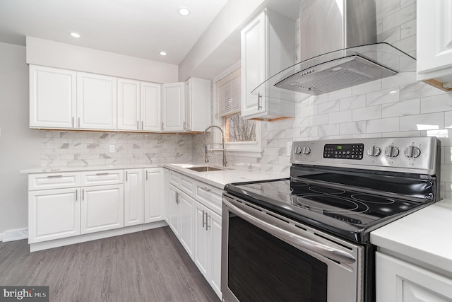 kitchen featuring wood finished floors, electric range, a sink, light countertops, and wall chimney exhaust hood