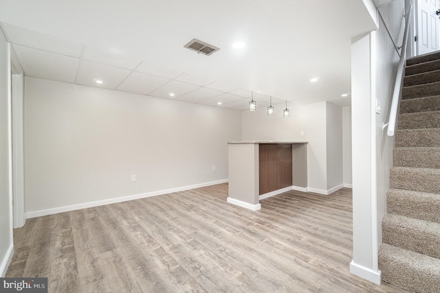 finished basement featuring visible vents, baseboards, stairs, light wood-style floors, and a dry bar