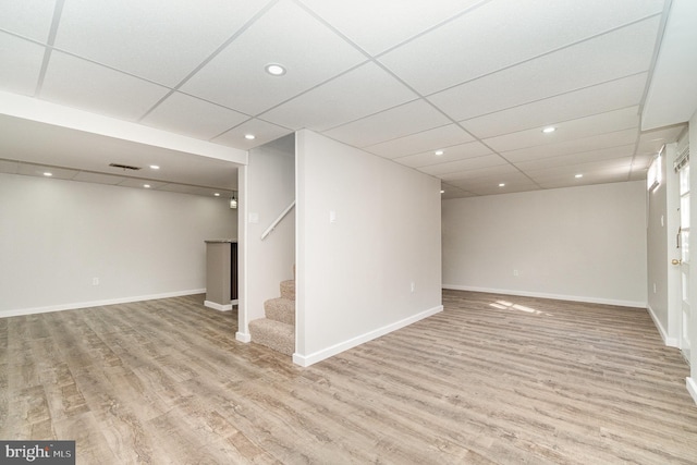 finished below grade area featuring stairway, a paneled ceiling, and wood finished floors