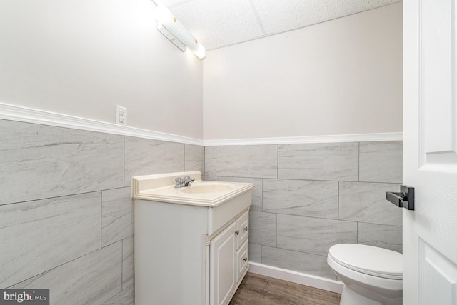 half bathroom featuring vanity, wood finished floors, wainscoting, tile walls, and toilet