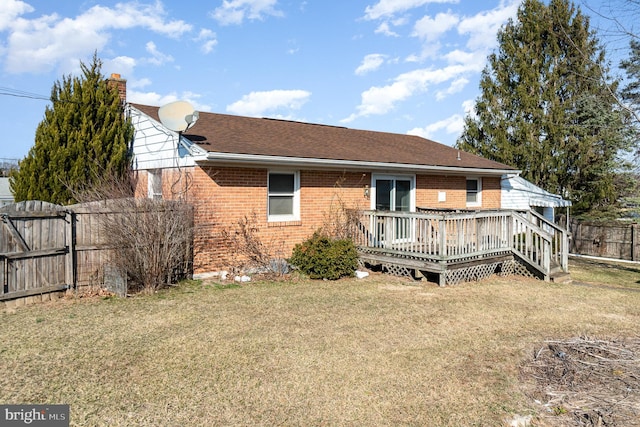 rear view of property with a lawn, a deck, fence, brick siding, and a chimney