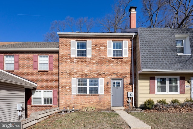 townhome / multi-family property featuring a chimney, a shingled roof, and brick siding