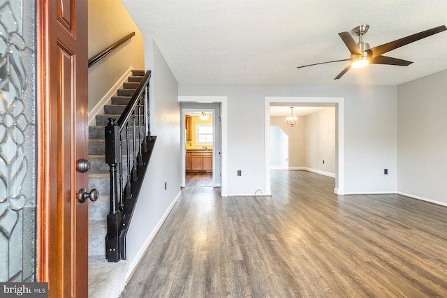 unfurnished living room with stairway, wood finished floors, baseboards, and ceiling fan