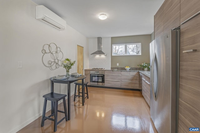 kitchen with baseboards, a wall mounted AC, stainless steel appliances, wall chimney range hood, and modern cabinets