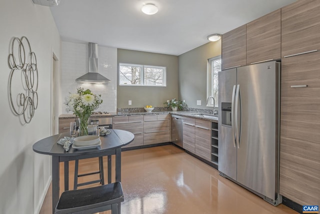 kitchen with stone counters, appliances with stainless steel finishes, modern cabinets, wall chimney exhaust hood, and a sink