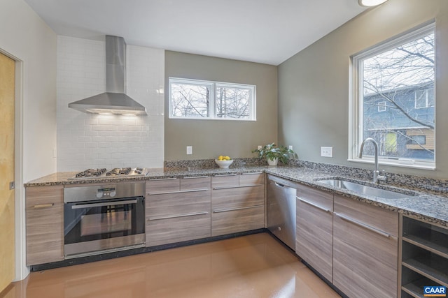 kitchen with a sink, stone countertops, appliances with stainless steel finishes, wall chimney range hood, and decorative backsplash