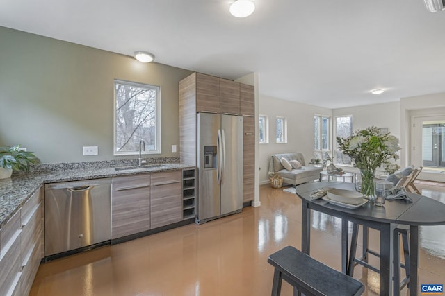 kitchen with light stone countertops, a sink, stainless steel appliances, modern cabinets, and brown cabinets