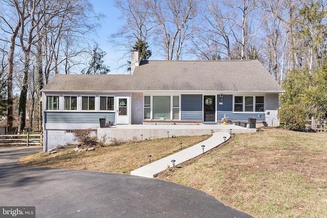 ranch-style house featuring a front lawn, fence, roof with shingles, and a chimney