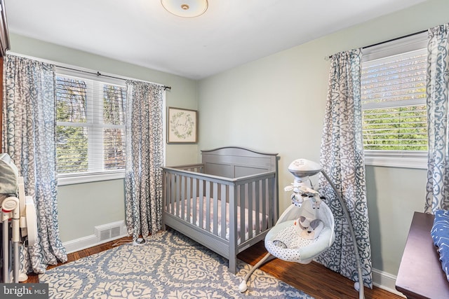 bedroom featuring visible vents, a nursery area, baseboards, and wood finished floors